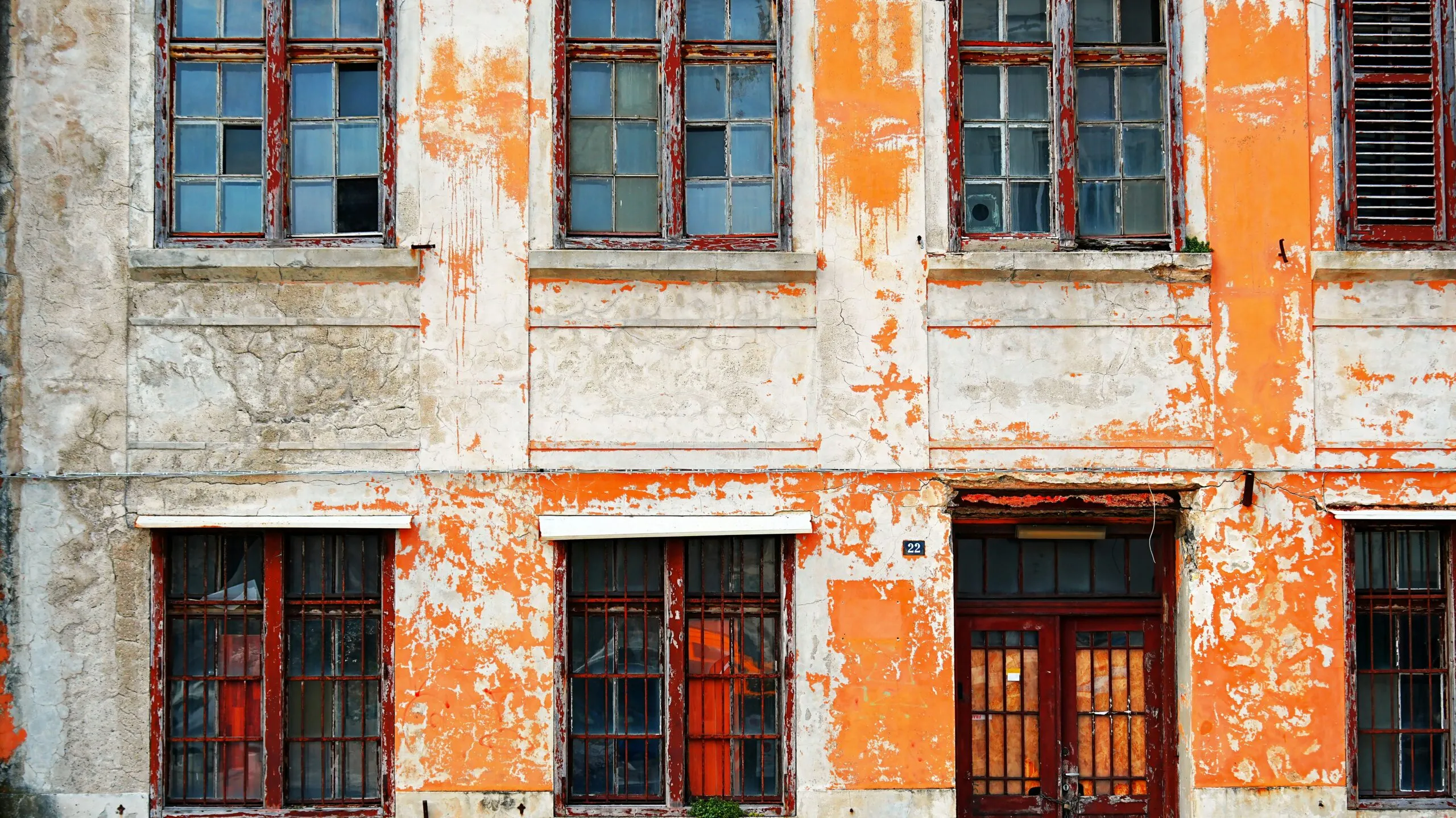 Old building facade with peeling orange paint and broken windows