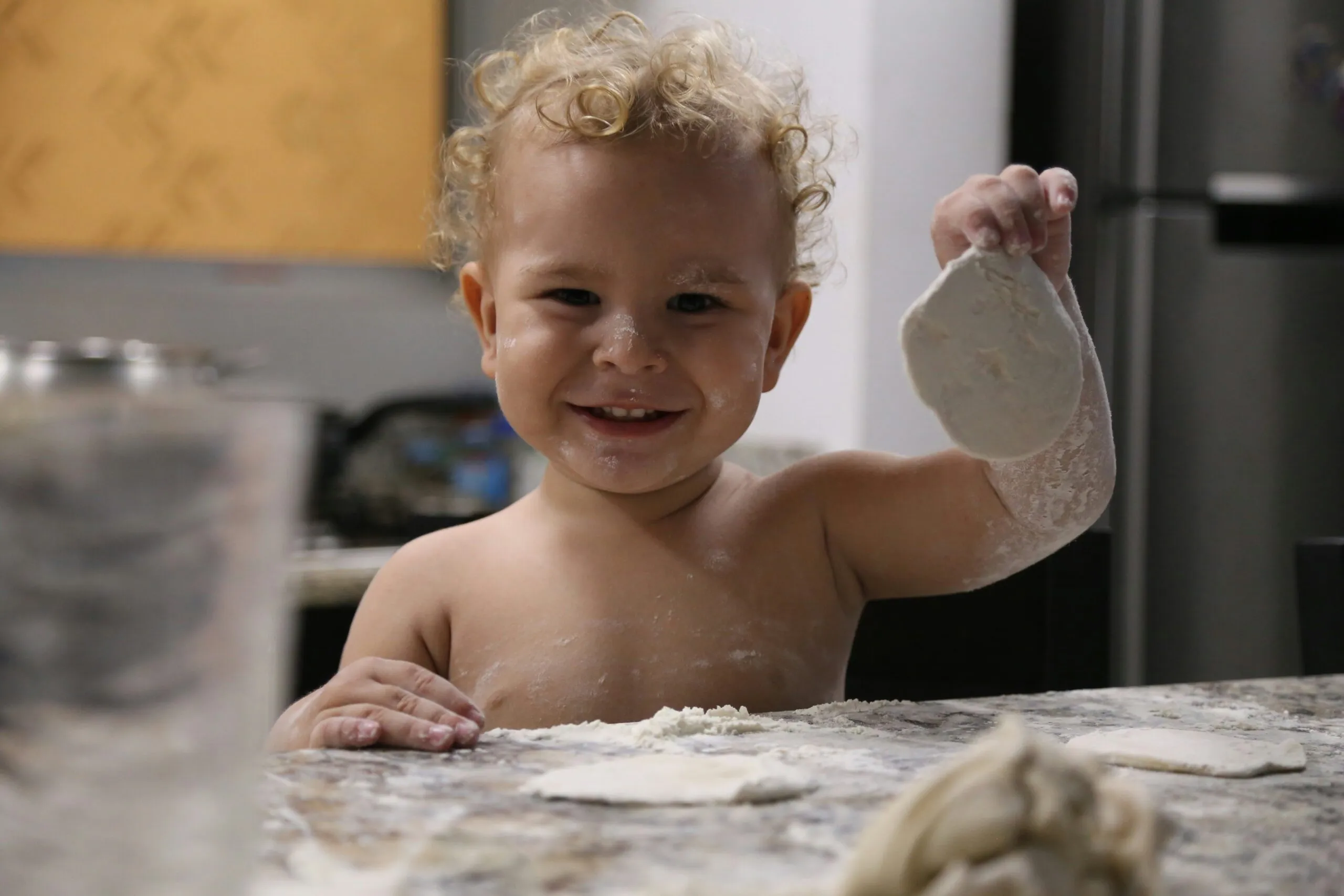 Happy toddler plays with dough in the kitchen.