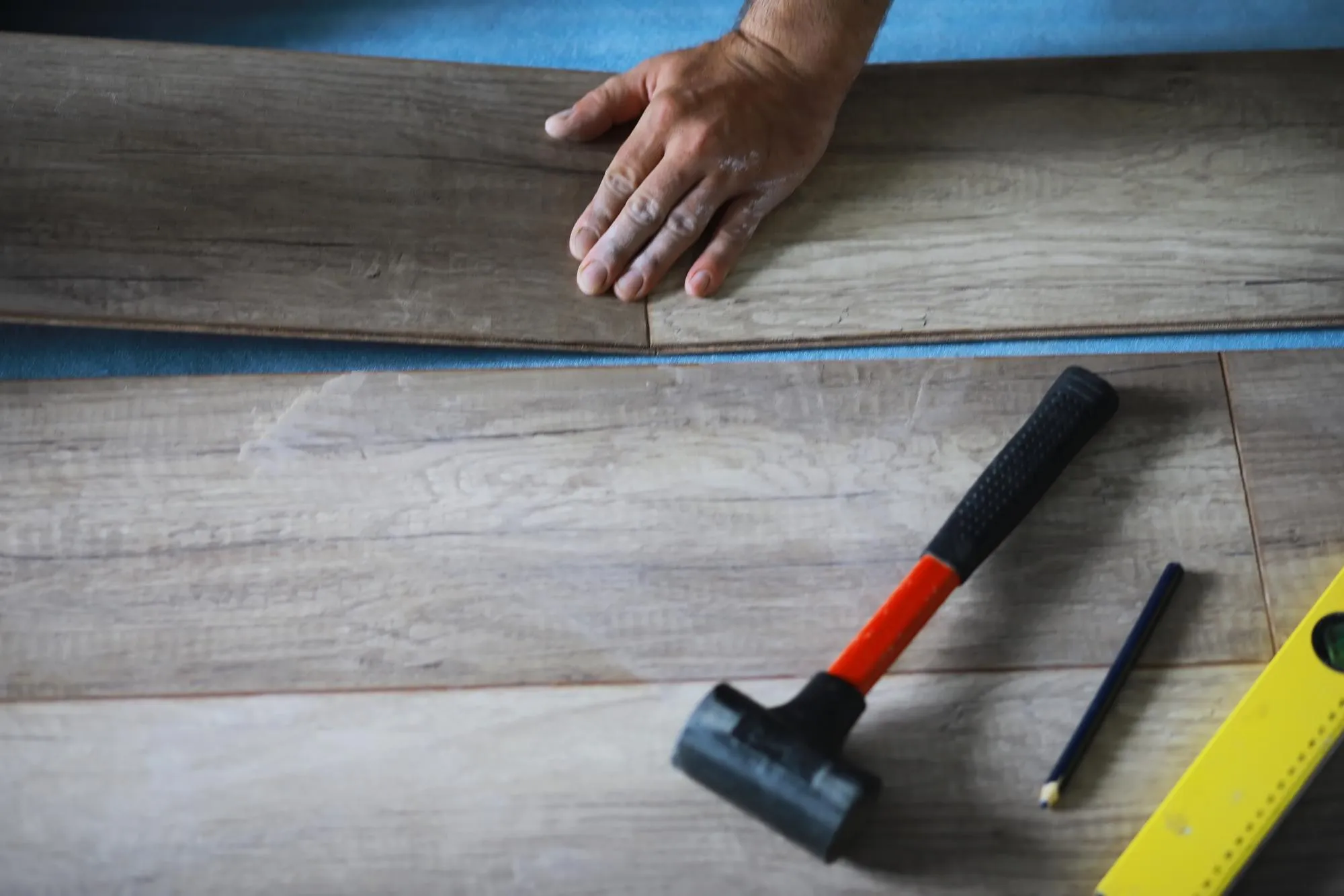 Installing laminated floor detail on man hands blue wooden tile over white foam base layer small pile with more tiles background