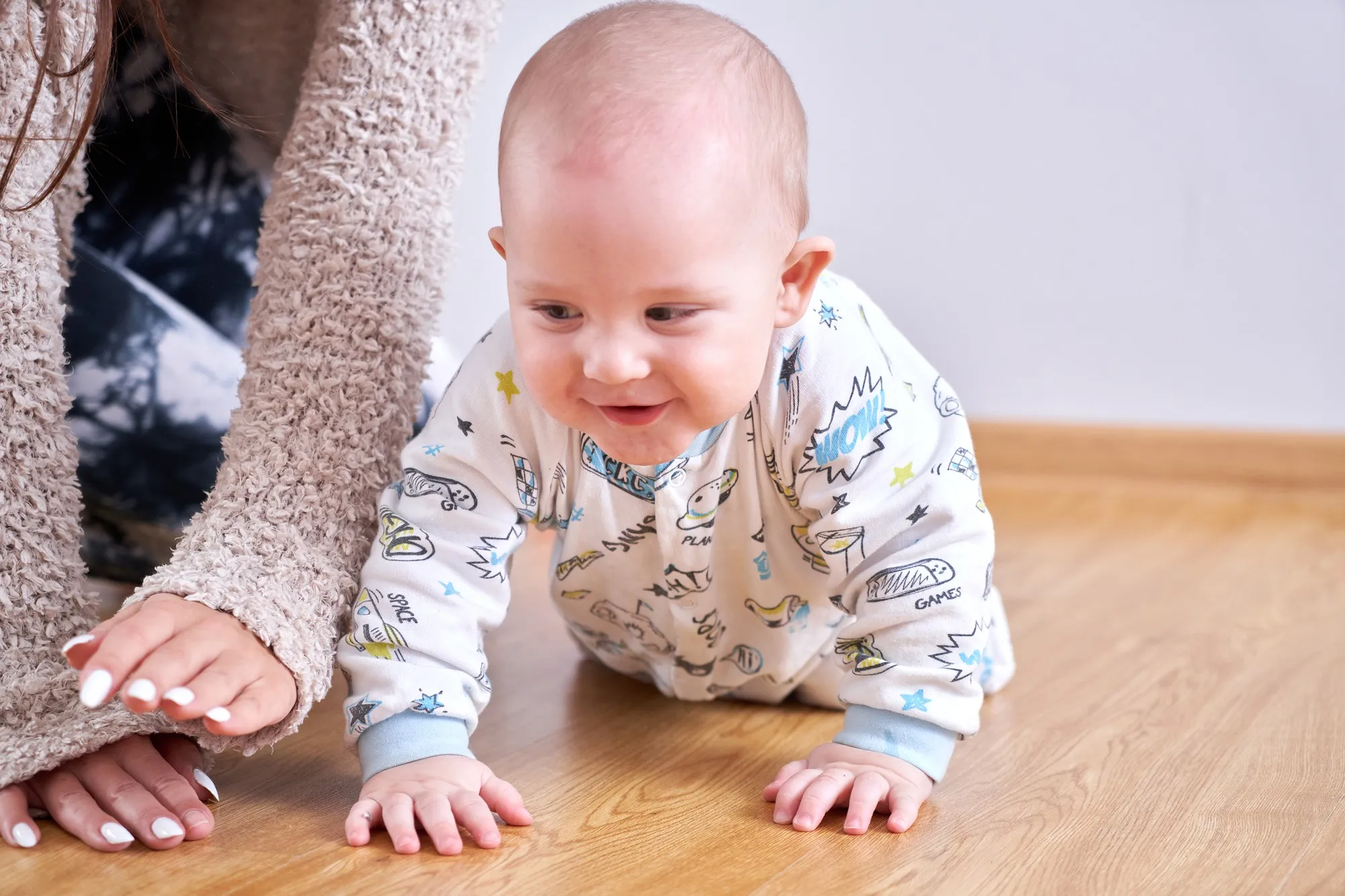 Mom plays with her toddler son at home on the floor, teaches to crawl, child's first steps, happy family