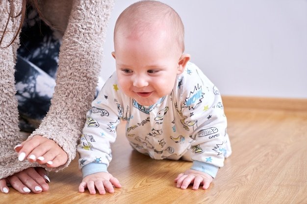 Mom plays with her toddler son at home on the floor, teaches to crawl, child's first steps, happy family