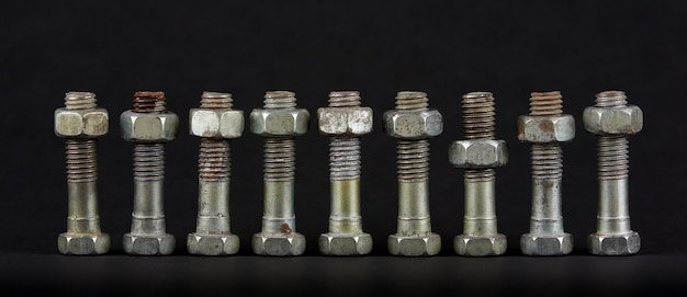 Nine bolts with nuts in a row on black background. One object differs from the rest in position. One nut is located below the others.