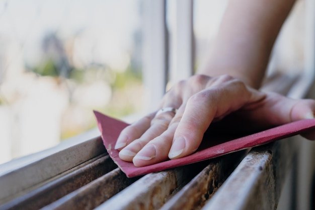 Normal view of a woman's hands sanding a window frame before painting Empowered woman concept