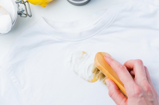 A person hand using a small brush rubbing powder baking soda on a yellow stain on white tshirt