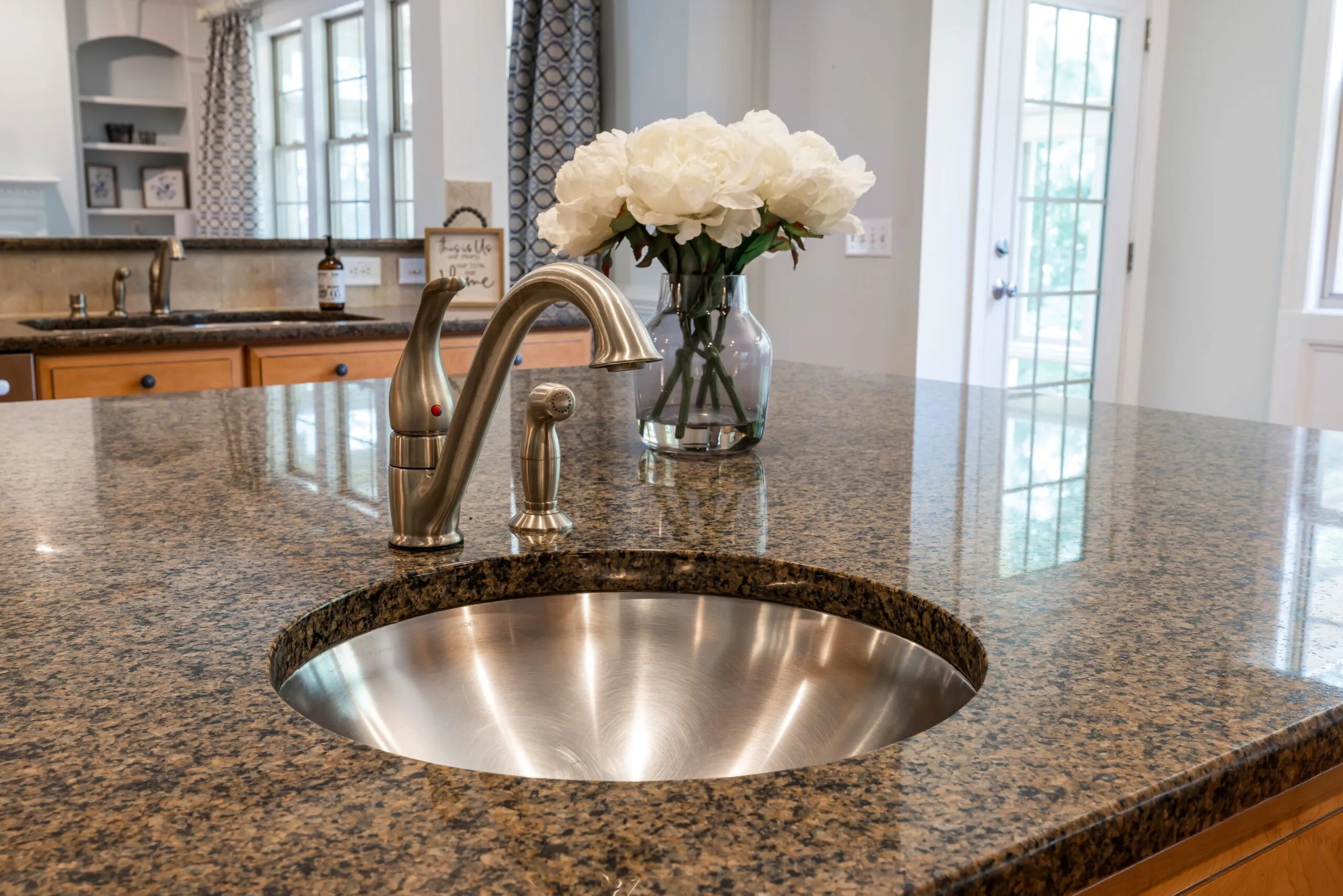 Stylish kitchen interior featuring granite countertop, stainless steel sink, and a vase of white peonies.