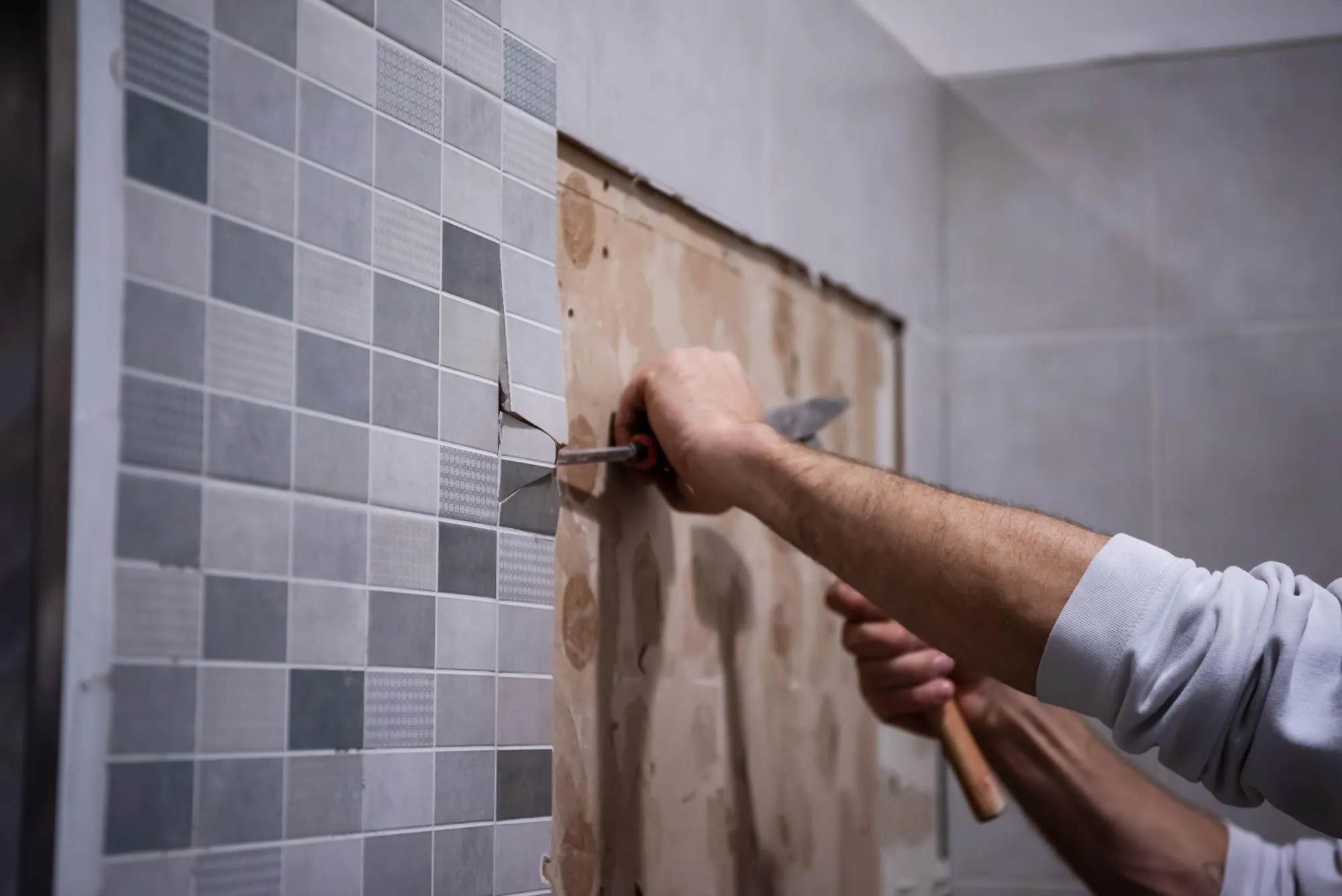 professional worker remove demolish old tiles in a bathroom with hammer and chisel