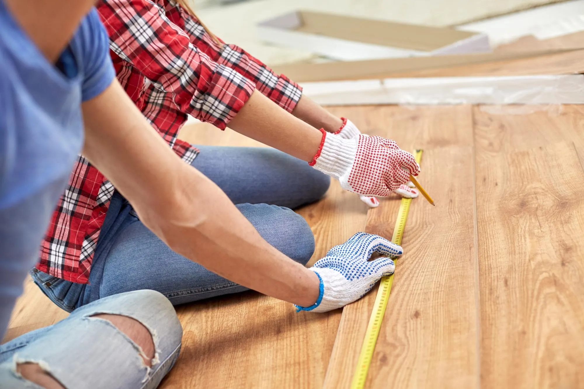 repair, building, flooring and people concept - close up of couple hands with ruler measuring parquet board at home