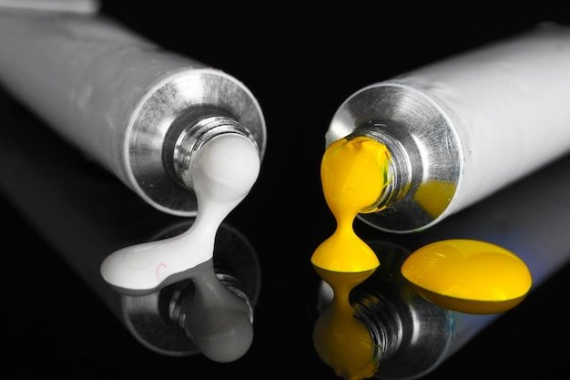 White and yellow paints follow from the tubes on black background closeup