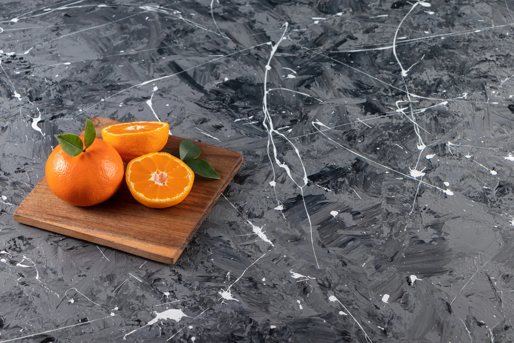 Whole fresh orange fruit with leaves placed on a wooden board