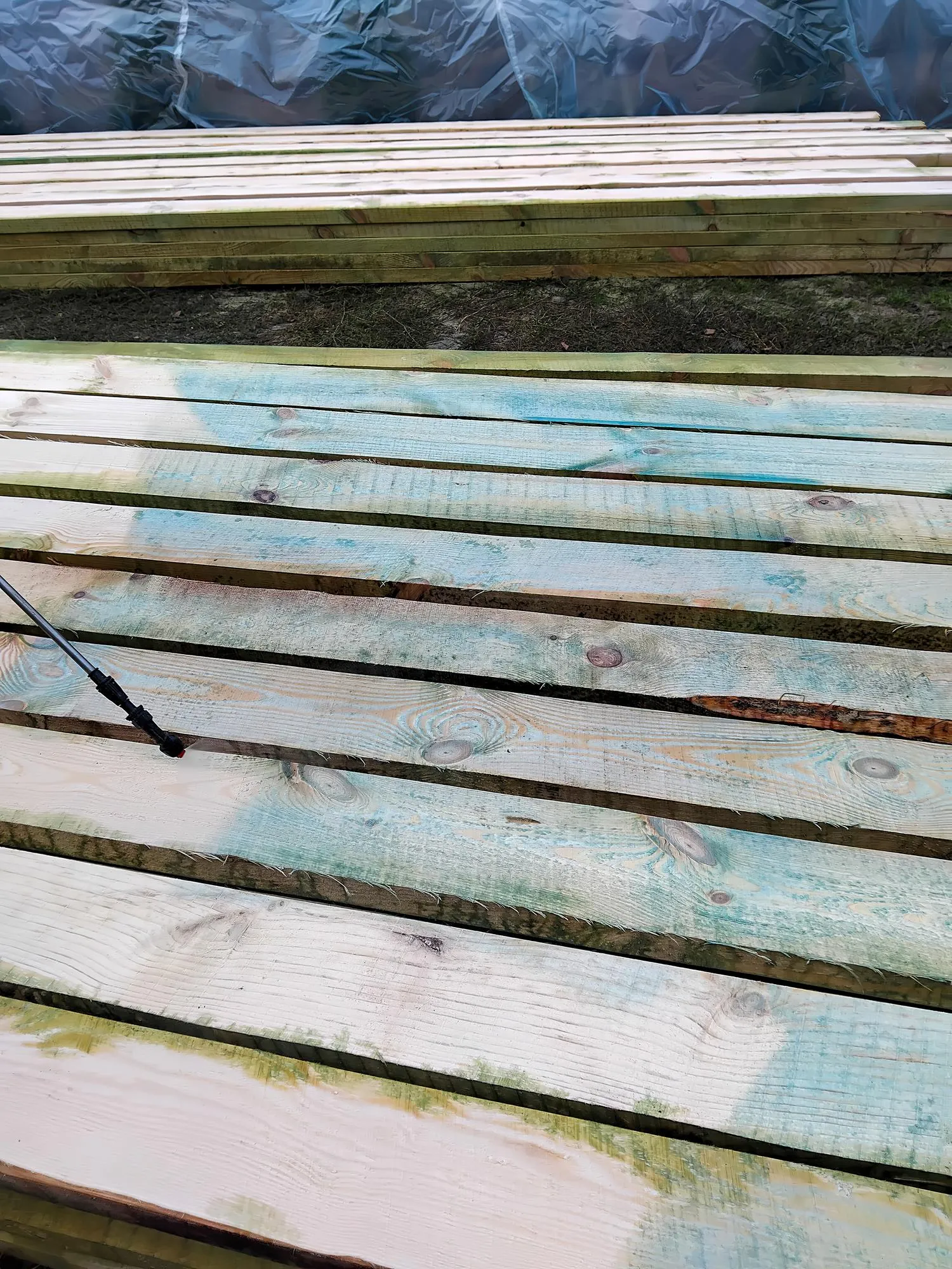 Wooden planks being prepared with a fresh coat of paint in an outdoor workspace