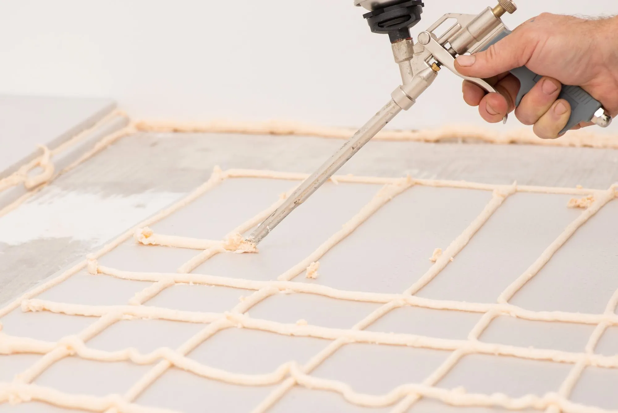 Worker applying foam with glue gun on sheet of styrofoam for gluing it to the floor in house