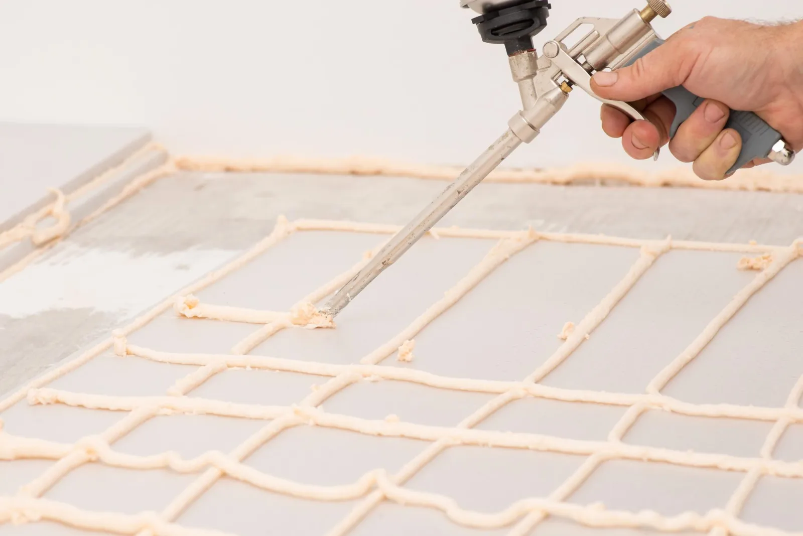 Worker applying foam with glue gun on sheet of styrofoam for gluing it to the floor in house
