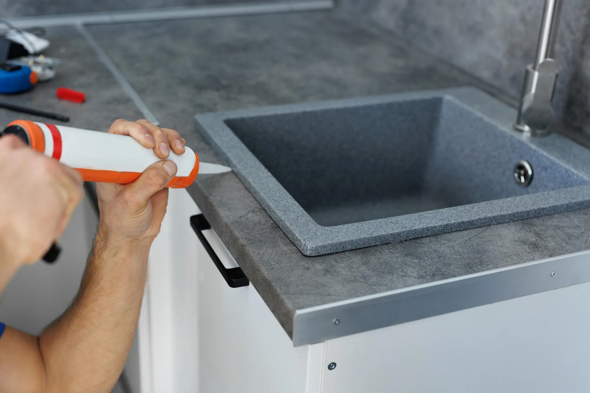 A worker seals up the kitchen sink with a sealant with a construction sealing gun