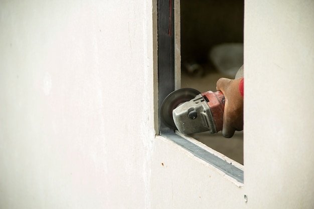 Worker using machine angle grinders at window edge cement board.
