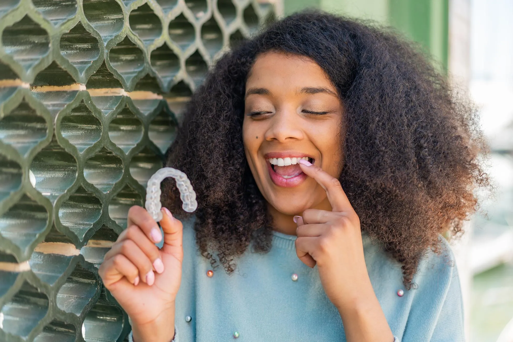 Young African American woman at outdoors holding invisible braces with happy expression