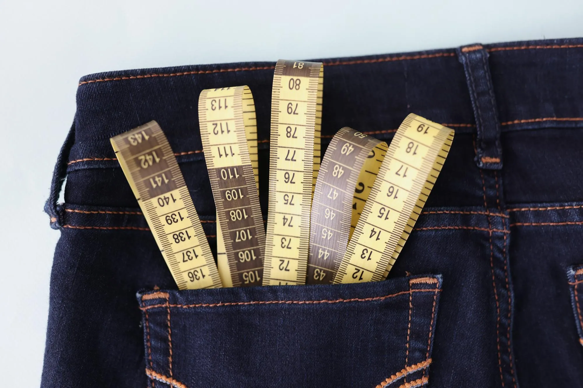 Close-up of yellow measuring tape in jeans pocket image of body slimming. Tool to measure body volume in atelier. Weight loss and weight control concept