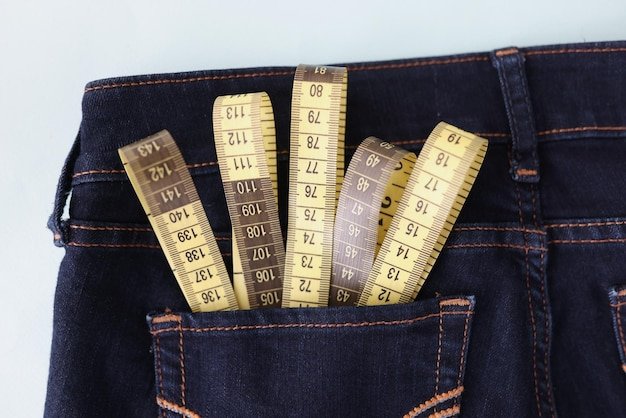Close-up of yellow measuring tape in jeans pocket image of body slimming. Tool to measure body volume in atelier. Weight loss and weight control concept