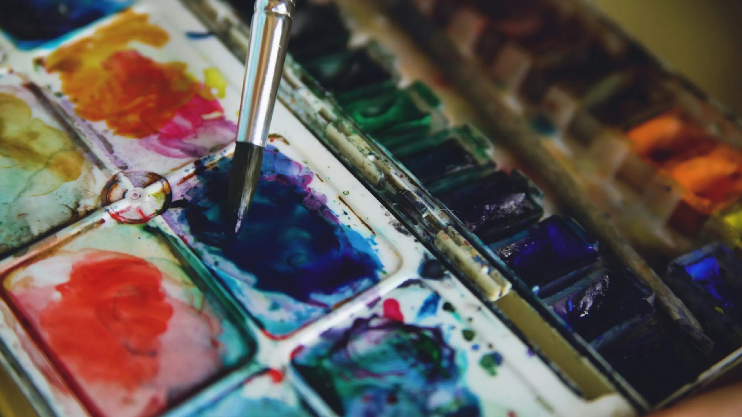 Artist dips brush into blue watercolor paint.