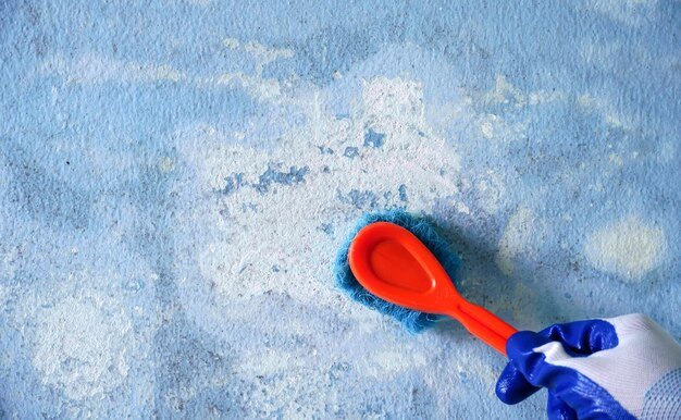 man wearing rubber gloves wipes the old cement wall dirty from the water leak with a brush