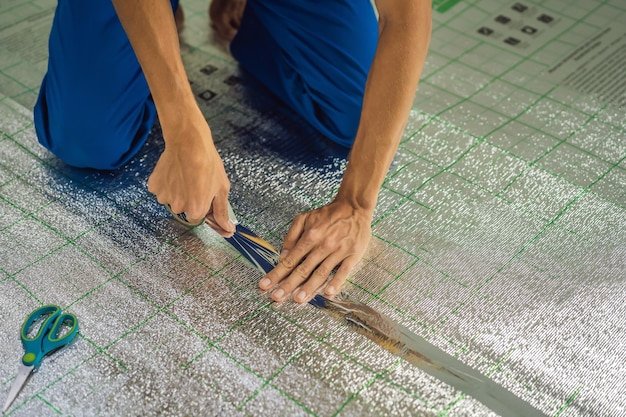 Master installs the overlapping thermal insulation in the room Floor heating installation Male hand holds reinforced tape Repair in the apartment floor insulation