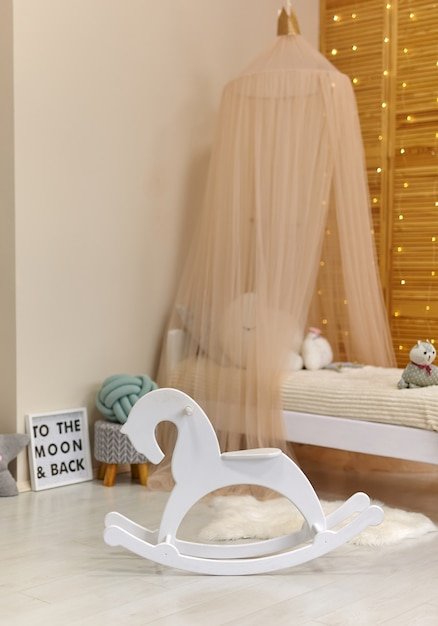 White wooden horse in Cute child's room interior with toys and modern furniture, bed with tent