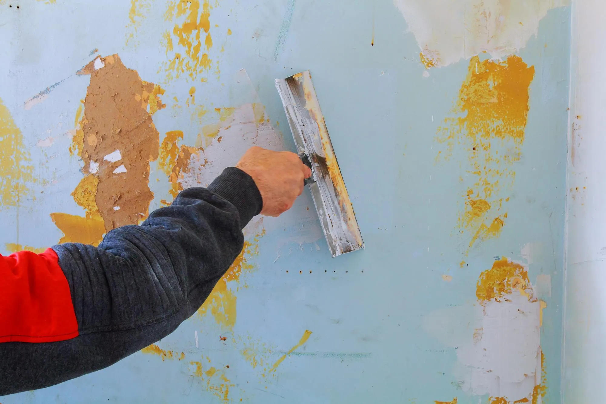Close-up of cropped hand scraping paint on wall