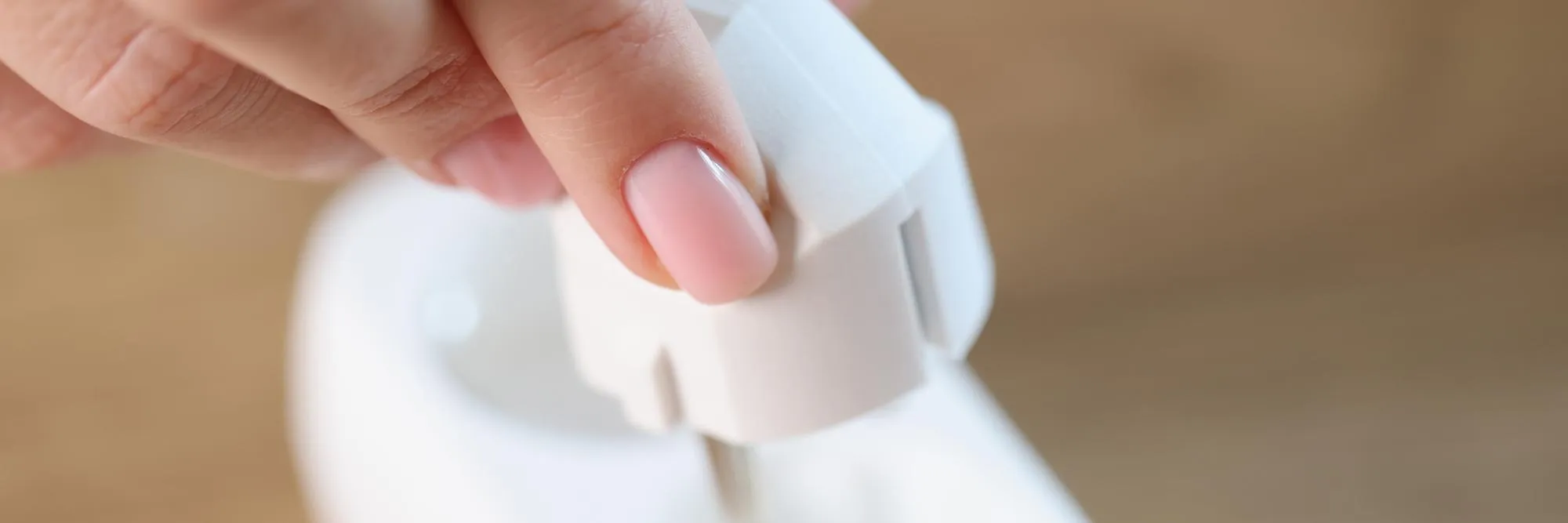 Closeup of female hand inserting electric plug into white socket connecting electrical devices