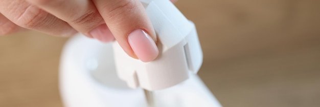 Closeup of female hand inserting electric plug into white socket connecting electrical devices