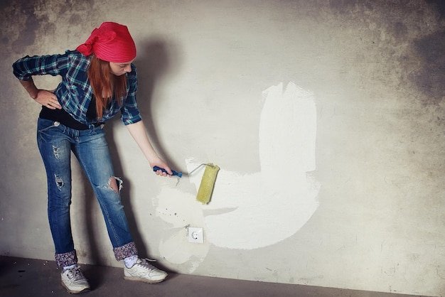 The girl is doing repairs in the apartment Home moving to a new apartment The worker makes repairs plastered and drills the wall