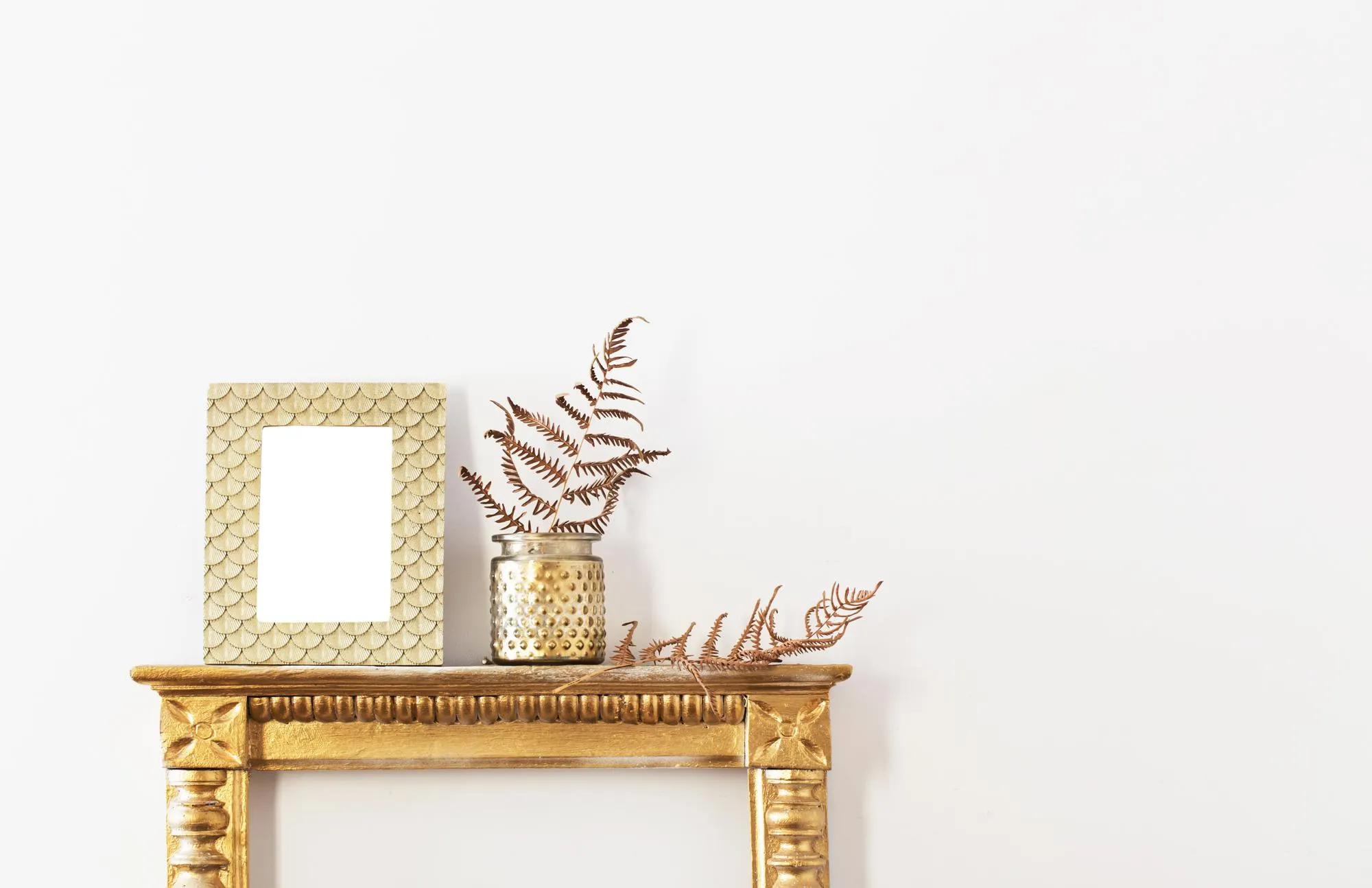 Golden frame and dried plants on white wall