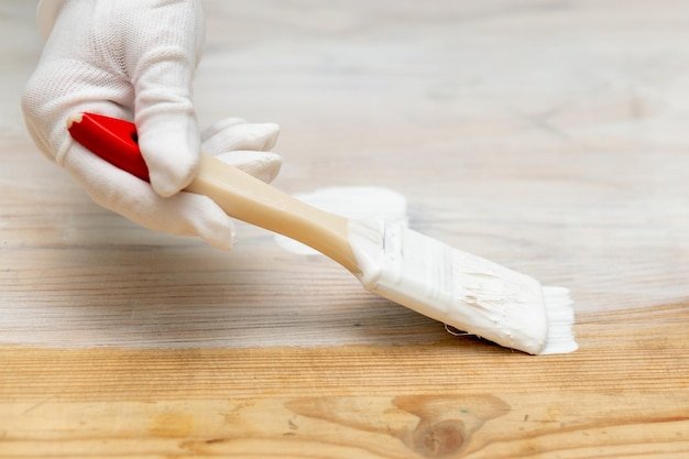 A hand in a protective glove with a brush paints wooden furniture