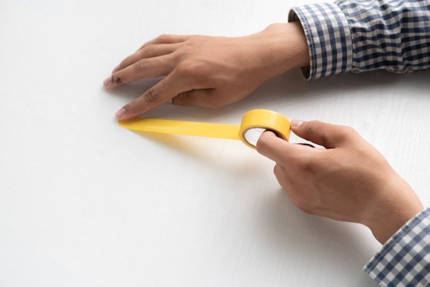 Hands holding an adhesive color tape and apply it to the white surface