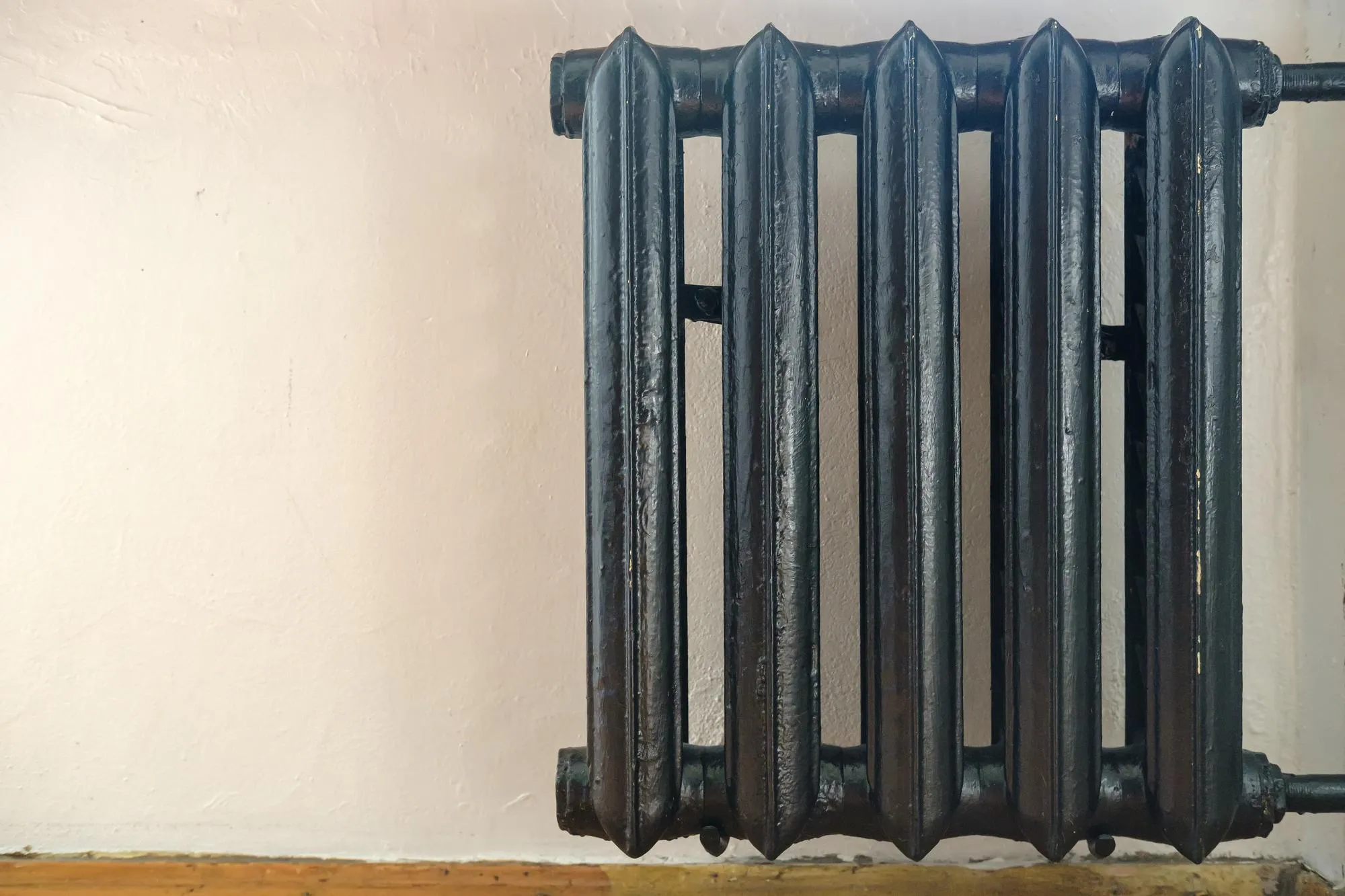 Old castiron radiator painted black against a white wall in the room
