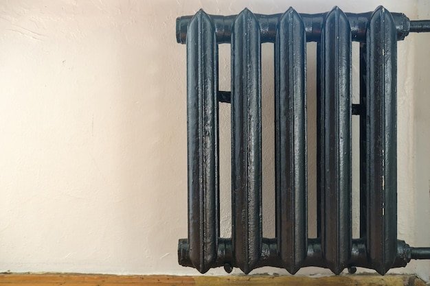 Old castiron radiator painted black against a white wall in the room