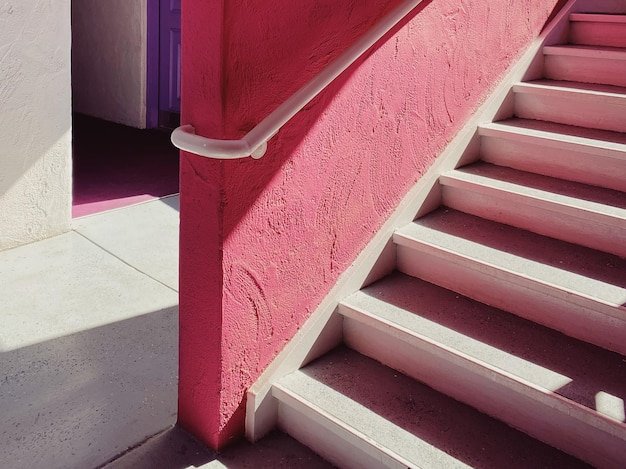 a pink stair case with a white handle and a purple door