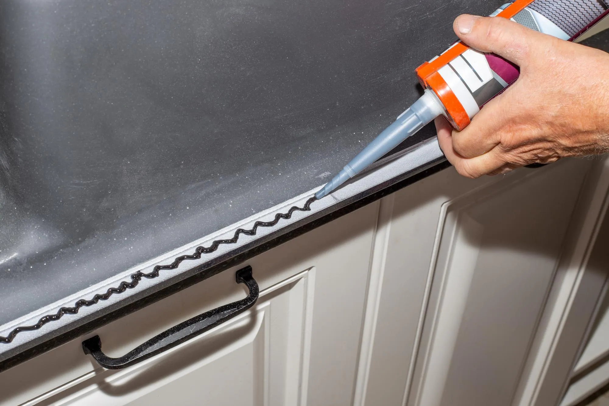 The plumber installs the sink Applying sealant to the rim of a kitchen sink for countertop installation