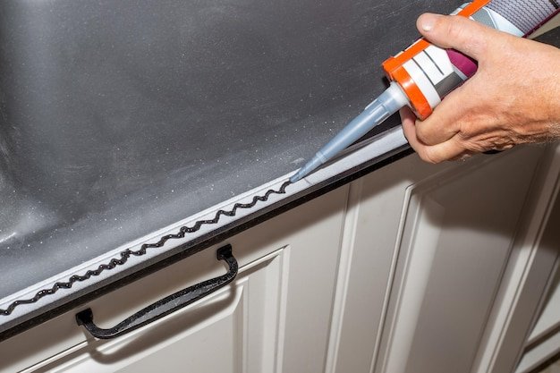 The plumber installs the sink Applying sealant to the rim of a kitchen sink for countertop installation