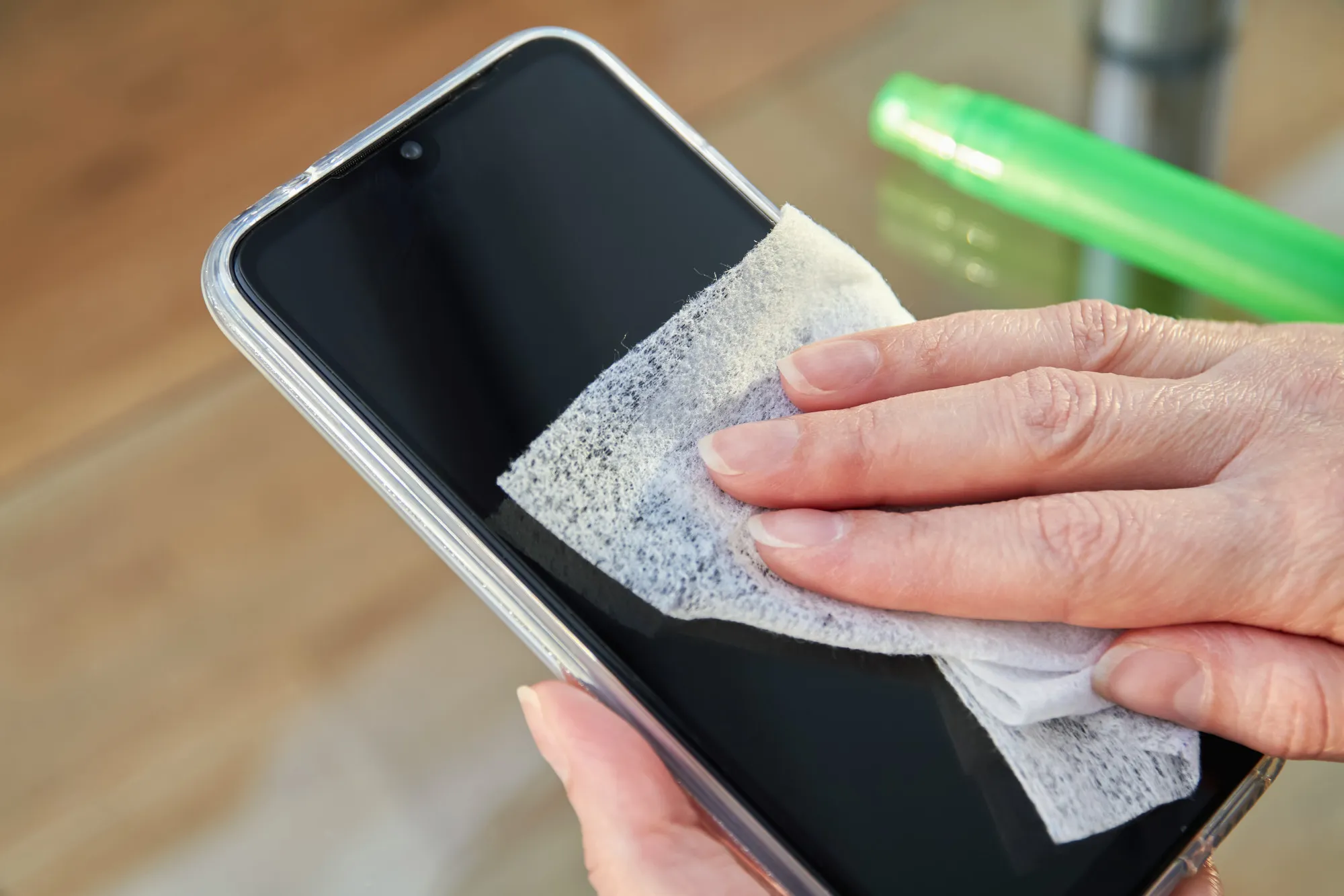 Woman is cleaning a smartphone with a jet of alcohol aerosol hand sanitizer and disposable cloth at home. Precautions regarding viruses
