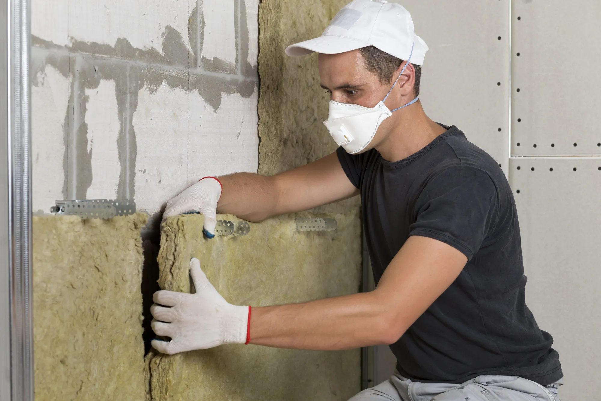 Worker in protective respirator mask insulating rock wool insulation in wooden frame for future house walls for cold barrier. Comfortable warm home, economy, construction and renovation concept