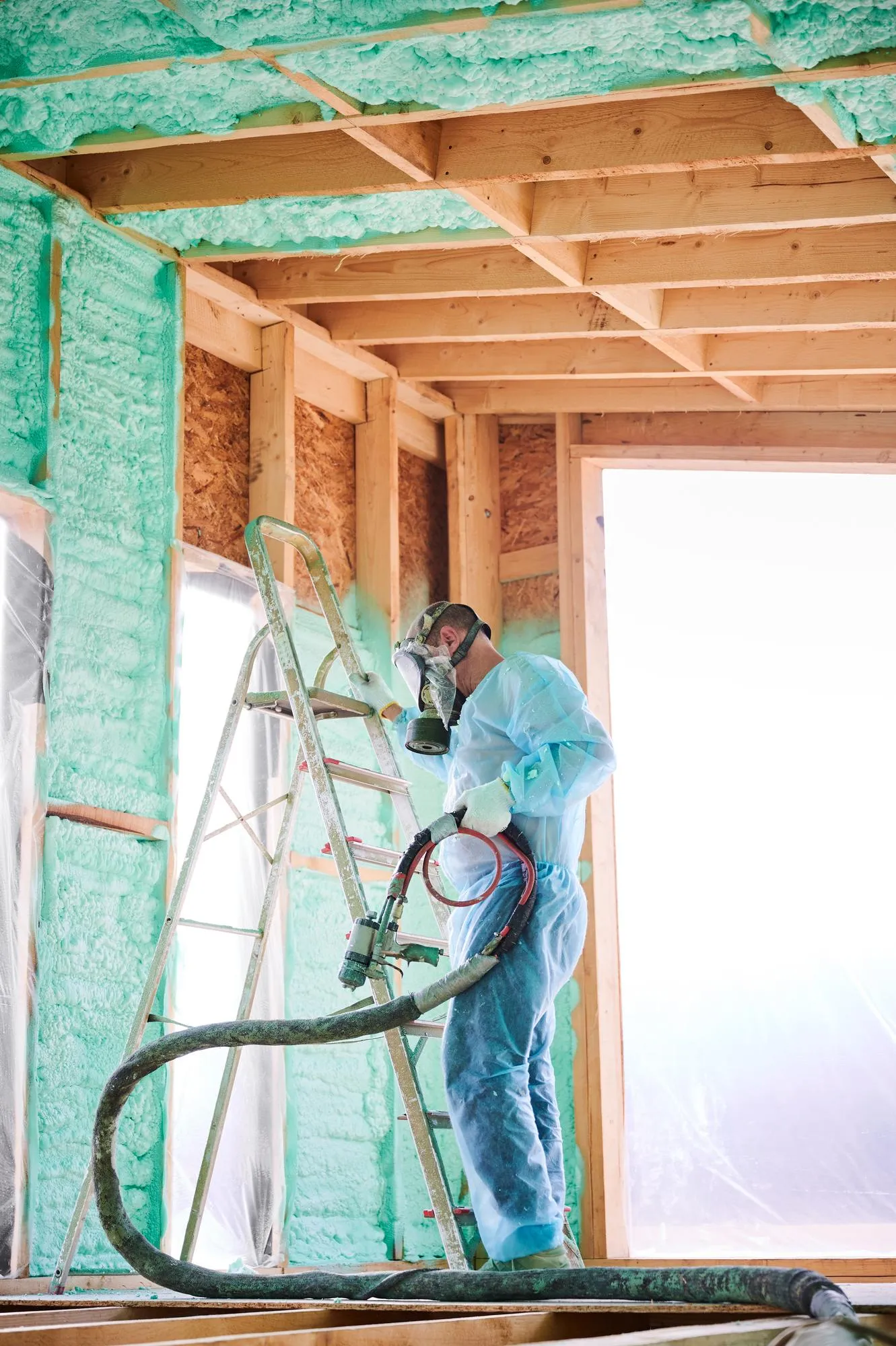 Worker spraying polyurethane foam for insulating wooden frame house
