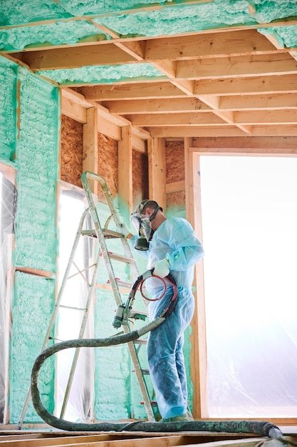 Worker spraying polyurethane foam for insulating wooden frame house