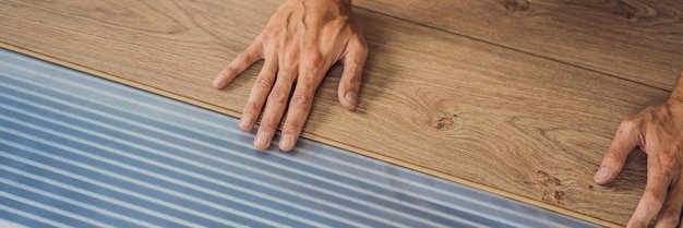 BANNER LONG FORMAT Man installing new wooden laminate flooring on a warm film floor Infrared floor heating system under laminate floor