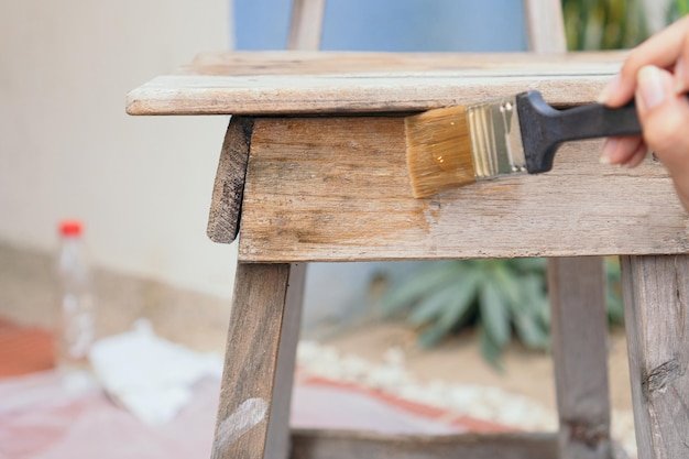 Close up photo of a young woman in the backyard paints an old chair