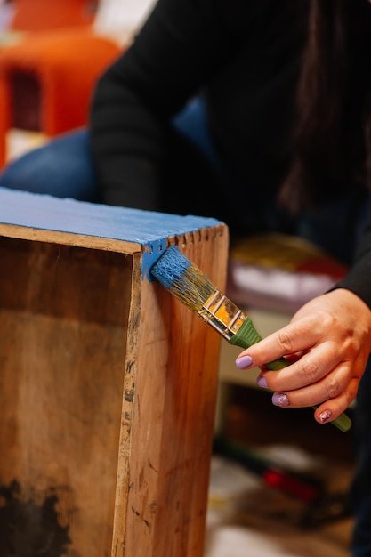 Closeup of lady holding brush carefully painting side part of old wooden closet drawer in bright blue color Reuse of old things Sustainable ecofriendly actions for planet future