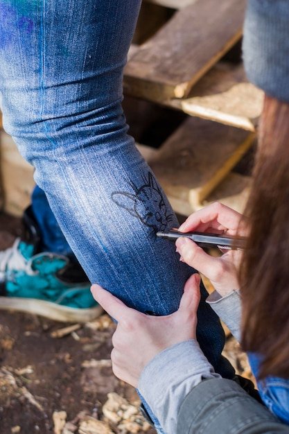Cropped hand of woman drawing on friend leg