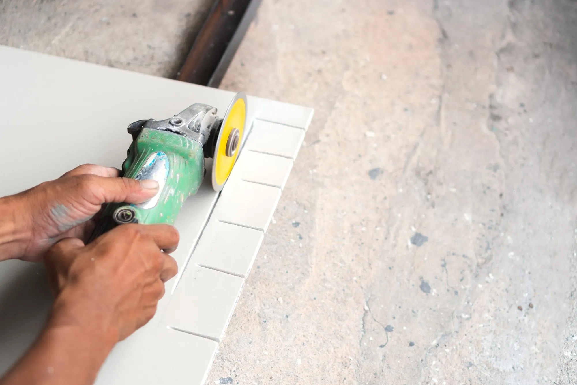 Cropped hands of manual worker cutting tile with electric saw at workshop