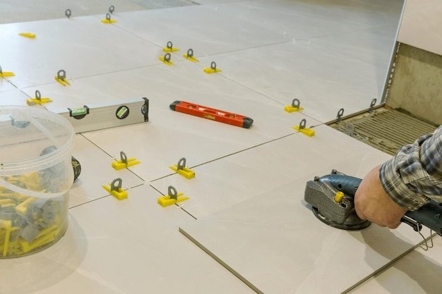The hands of the tiler are laying the ceramic tile on the floor