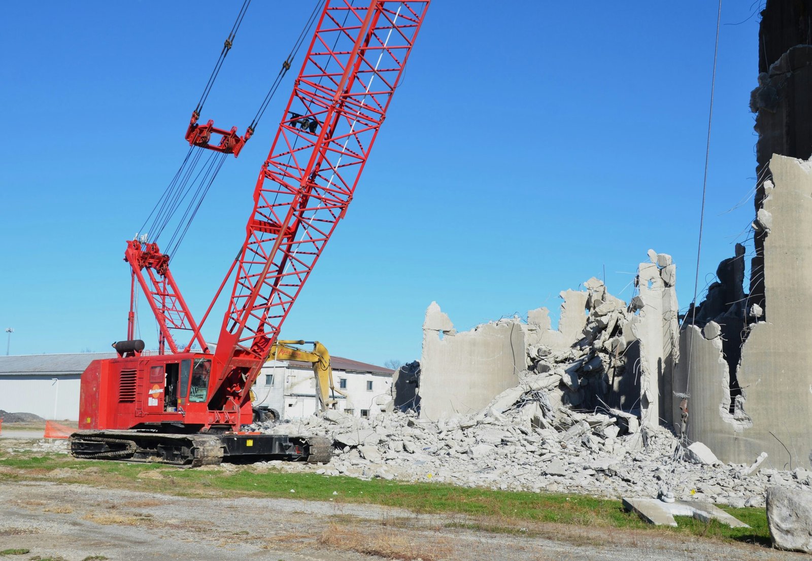 Crane demolishing concrete building with debris pile.