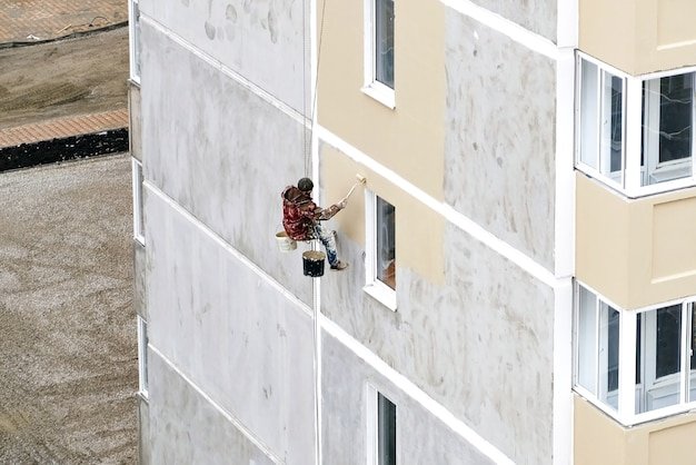 Industrial rope access worker hanging from the building while painting the exterior facade wall. Industrial alpinism concept image.