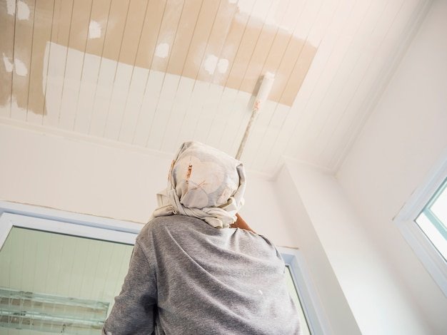 Partial focus photo of a man is painting ceiling using roller brush